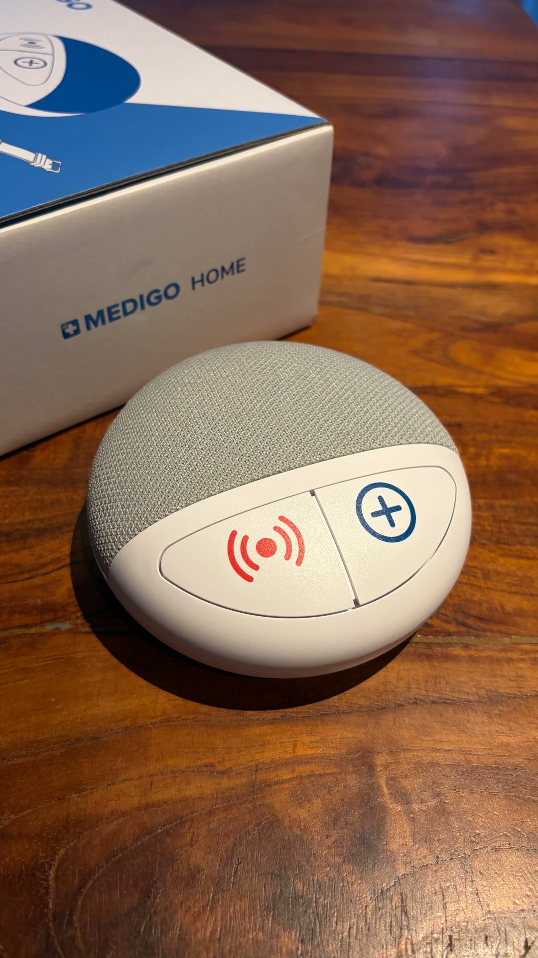 Der Medigo HOME neben seiner blau-weißen Verpackung auf einem Holztisch